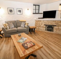 A living room with grey sofas wooden tables a television on a stone fireplace at Ellie's Cottage in Burford