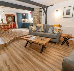 A living room with two grey sofas a wooden coffee table and side table dining table with chairs and blue kitchen cabinets at Ellie's Cottage in Burford