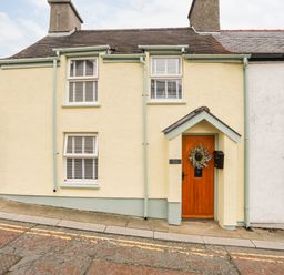 Exterior view of a yellow cottage with a wooden door and two windows at Bwthyn Lili (Lily Cottage) in Cemaes Bay