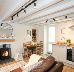 A kitchen and dining area with a wood burner fireplace and wooden table with chairs at Bwthyn Lili (Lily Cottage) in Cemaes Bay