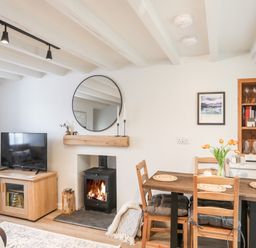 A living room with a wood stove next to a dining table with four chairs and a TV on a wooden cabinet at Bwthyn Lili (Lily Cottage) in Cemaes Bay