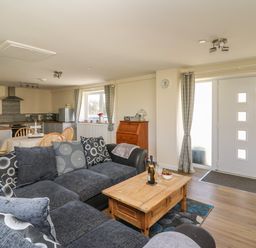A living room with a dark sofa and wooden coffee table next to a front door and an open kitchen with a dining table at Brynteg Cottage in Tegryn