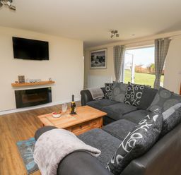 A living room with a black sectional sofa a wooden coffee table and a wall-mounted television at Brynteg Cottage in Tegryn