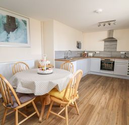 A kitchen with wooden table and chairs a tablecloth and a framed picture on the wall at Brynteg Cottage in Tegryn