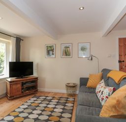 A living room with a gray sofa yellow cushions a patterned rug a wooden TV stand with a television and framed pictures on the wall at Nuthatch in Honiton