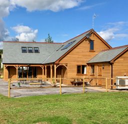 A wooden house with a slate roof and outdoor seating area surrounded by a wooden fence at Riverside Lodge in Washford