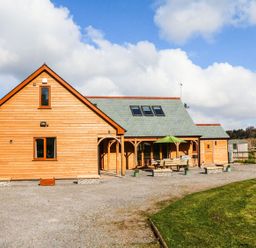 A wooden house with a gabled roof skylights and an outdoor seating area with an umbrella at Riverside Lodge in Washford