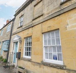 A row of stone buildings with blue windows and doors along a sidewalk in Lower Pack Horse Cottage in Winchcombe
