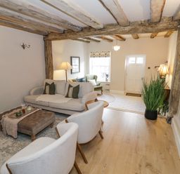 A living room with sofas chairs ottoman wooden beams and a plant at Lower Pack Horse Cottage in Winchcombe