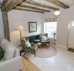 A sitting room with beige sofa green armchairs round rug and exposed wooden beams at Lower Pack Horse Cottage in Winchcombe