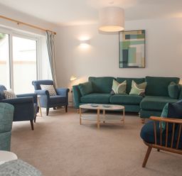 A living room with a green sofa blue armchairs wooden framed chair coffee table and wall art at Brooklands in Uplyme