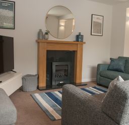 A living room with a grey sofa and teal sofa around a fireplace with a round mirror above at Brooklands in Uplyme