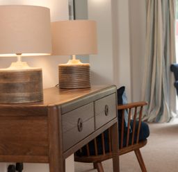 A wooden side table with two table lamps next to a wooden chair and a blue armchair in a room at Brooklands in Uplyme