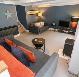 A living room with two sofas a television a lamp and stairs at Winterbrook Cottage in Mevagissey