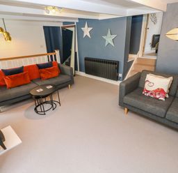 A living room with two gray sofas one with red and blue cushions and the other with octopus design cushions a black stove and blue walls at Winterbrook Cottage in Mevagissey