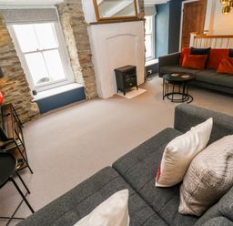 A living room with two gray sofas, a small black wood stove, two windows with stone surrounds and a TV on a stand at Winterbrook Cottage Mevagissey