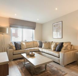 A living room with a beige sectional sofa a coffee table with decorative vases a floor lamp and a table lamp at Sans Souci in Seahouses
