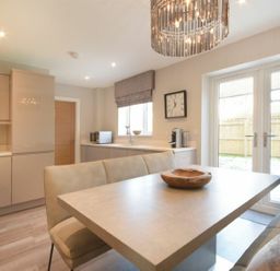 A kitchen with a dining table and bench seating a clock on the wall and glass doors leading outside at Sans Souci in Seahouses