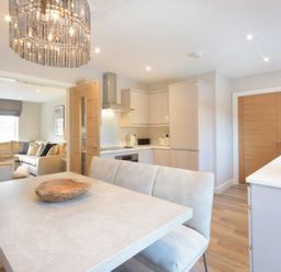 A kitchen and dining area with a table and cushioned bench and a living room with sofas at Sans Souci in Seahouses