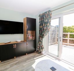 A living area with a wall-mounted TV and black cabinets next to sliding glass doors with floral curtains at Rose Lodge in High Newton-by-the-Sea near Embleton