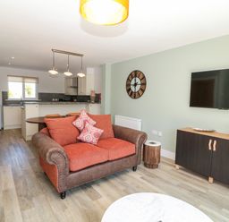 A living room with an orange and brown sofa a wall clock and a flat screen tv at Rose Lodge in High Newton-by-the-Sea near Embleton