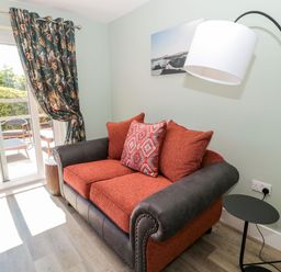 A sofa with cushions next to a floor lamp and a sliding glass door with curtains at Rose Lodge in High Newton-by-the-Sea near Embleton