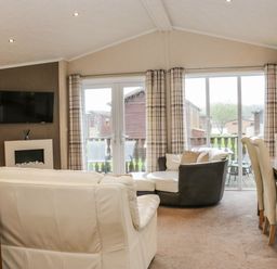 A living room with sofas a wall mounted television a dining table and chairs and large windows with curtains at Walkers Rest in Warton near Carnforth