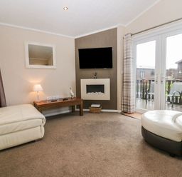 A living room with cream sofas wooden coffee table wall mounted television and glass doors leading outside at Walkers Rest in Warton near Carnforth