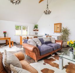 A living room with leather sofas, a glass coffee table with yellow flowers, and a dining area with wooden table and benches at Polly's Annexe in Levington