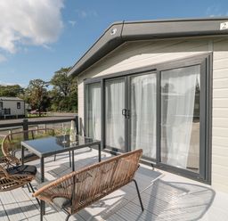 A patio with a table and chairs outside a mobile home with sliding glass doors at The Olive Lodge 227 Sycamore in New Milton