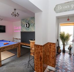 A game room with a pool table a television wooden benches and stools a guitar and a plant near a window at The Old Station House in Withernsea