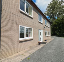 The exterior of a two-story brick house with several windows a white front door and a gravel driveway with trees in the background at Hillside Lodge in Newtown