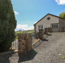 A gravel driveway with stone pillars and metal gate leading to a house with a circular window at Hillside Lodge in Newtown
