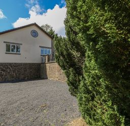 A house with stone and brick walls next to a gravel area and tall green bushes at Hillside Lodge in Newtown