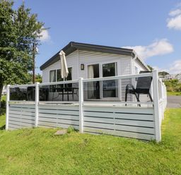 A white mobile home with a glass railing deck and outdoor furniture on grass at Olivias Haven in Wemyss Bay