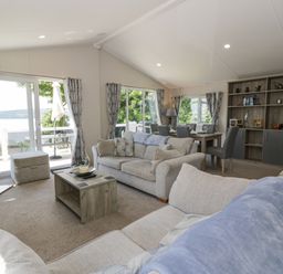 A living room with sofas coffee table tv dining table and chairs with windows showing outdoor view at Olivias Haven in Wemyss Bay