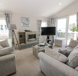 A living room with two sofas a coffee table a TV a fireplace and windows at Olivias Haven in Wemyss Bay