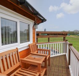 A wooden balcony with two wooden chairs and a table overlooking a green field at Dragonfly Retreat in Upper Marham