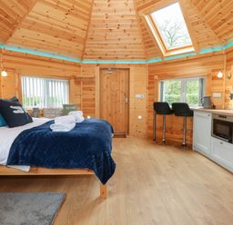 A wooden room with a bed kitchen area two stools and a skylight at Dragonfly Retreat in Upper Marham