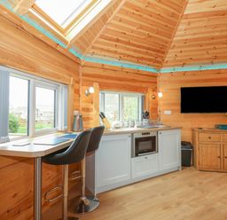 A kitchen area with bar stools countertop microwave and wall mounted television at Dragonfly Retreat in Upper Marham