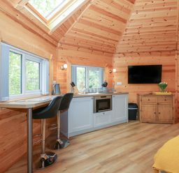 A kitchen area with bar stools oven and a wooden cabinet with a television mounted above at Honeybee Retreat in Pentney near Upper Marham