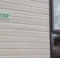 The exterior wall of a building with a house number 24 and tiptoes lodge sign next to a window reflecting trees and sky at Tiptoes Lodge in Carnforth