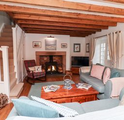 A living room with a wood beam ceiling a fireplace a plaid rocking chair a blue sofa a wooden coffee table and stairs at Seahares in Seahouses