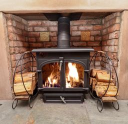 A lit wood burning stove with firewood on metal racks inside a brick fireplace at Seahares in Seahouses