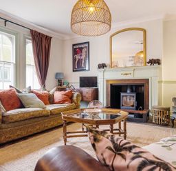 A living room with sofas, a fireplace, a mirror above it, a wooden coffee table, and framed pictures at Clematis House in St Columb Major