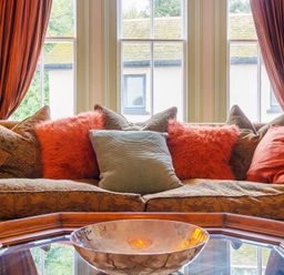 A sofa with multiple pillows in front of windows with curtains at Clematis House in St Columb Major