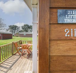 A wooden deck with a table and chairs outside wooden cabins at Little Trebah Atlantic Bays Holiday Park near St Merryn