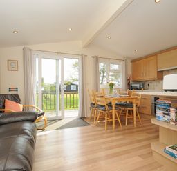 A living room with a black leather sofa and wooden dining table next to kitchen cabinets at Little Trebah Atlantic Bays Holiday Park near St Merryn