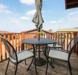 A balcony with a round table and four chairs with cushions and an umbrella at Seascape Retreat in Ilfracombe