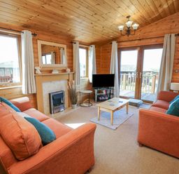 A living room with two orange sofas a wooden coffee table a fireplace a TV and windows with curtains at Seascape Retreat in Ilfracombe